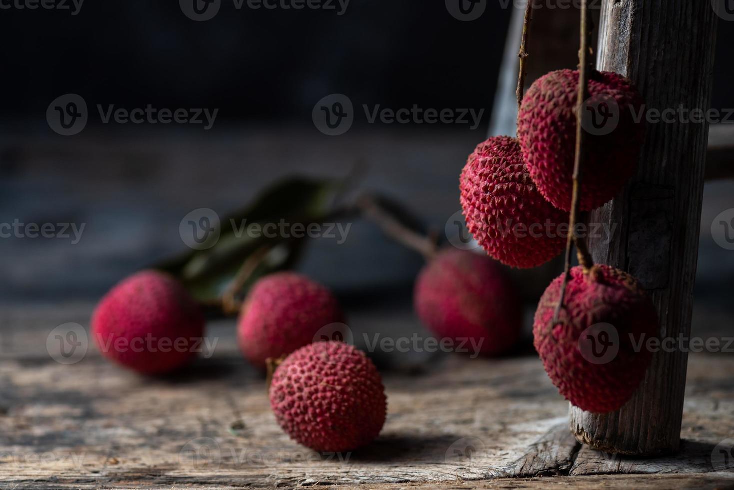 litchi läggs i en träplatta, skalad eller oöppnad, på ett mörkt träkornbord foto