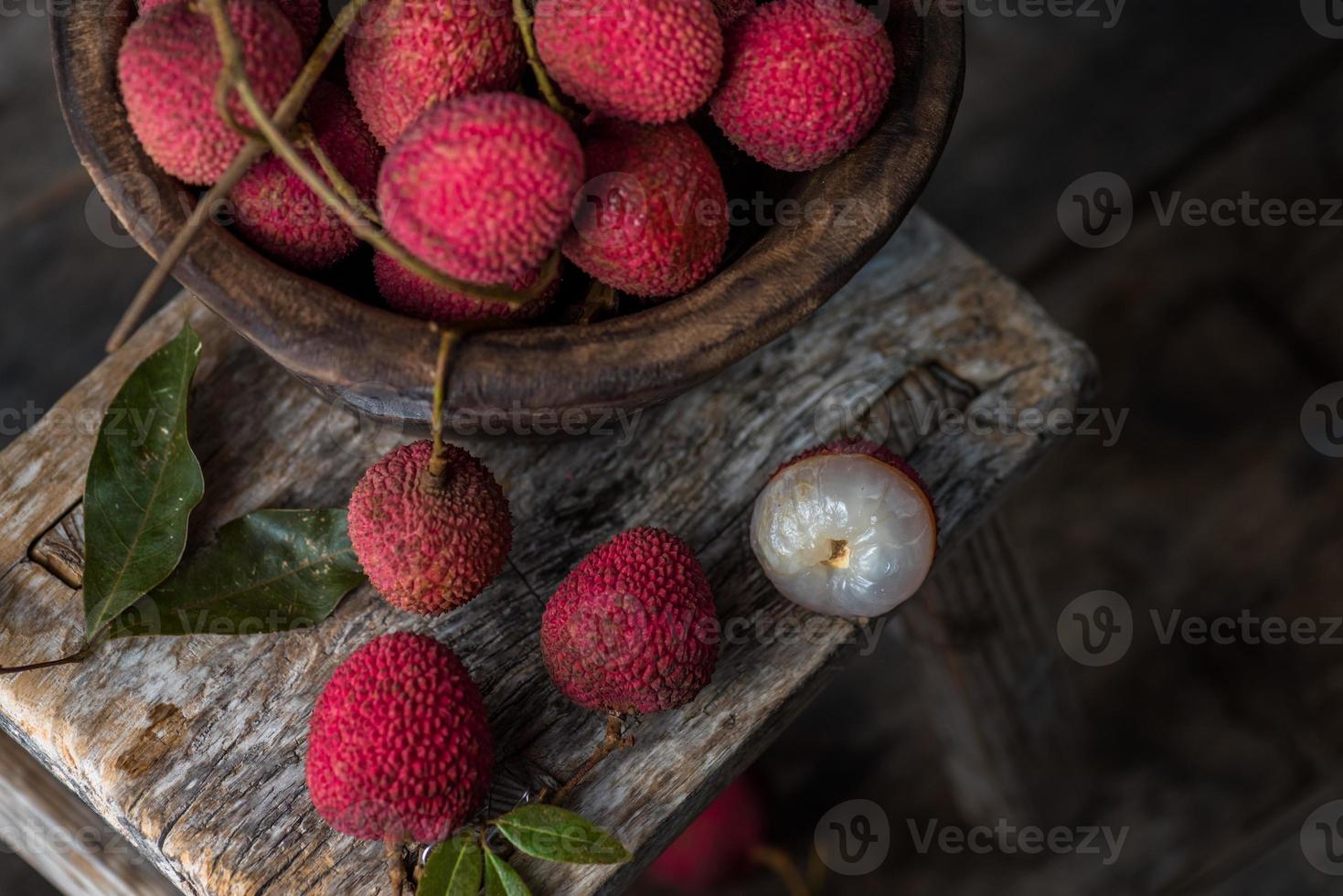 litchi läggs i en träplatta, skalad eller oöppnad, på ett mörkt träkornbord foto