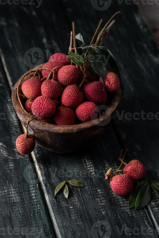 litchi läggs i en träplatta, skalad eller oöppnad, på ett mörkt träkornbord foto