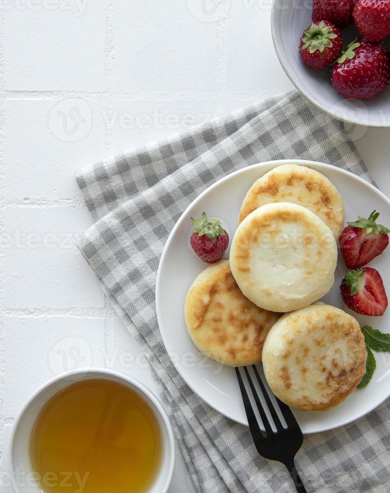 keso, pannkakor, ricottafritter på keramisk tallrik med färsk jordgubbe foto