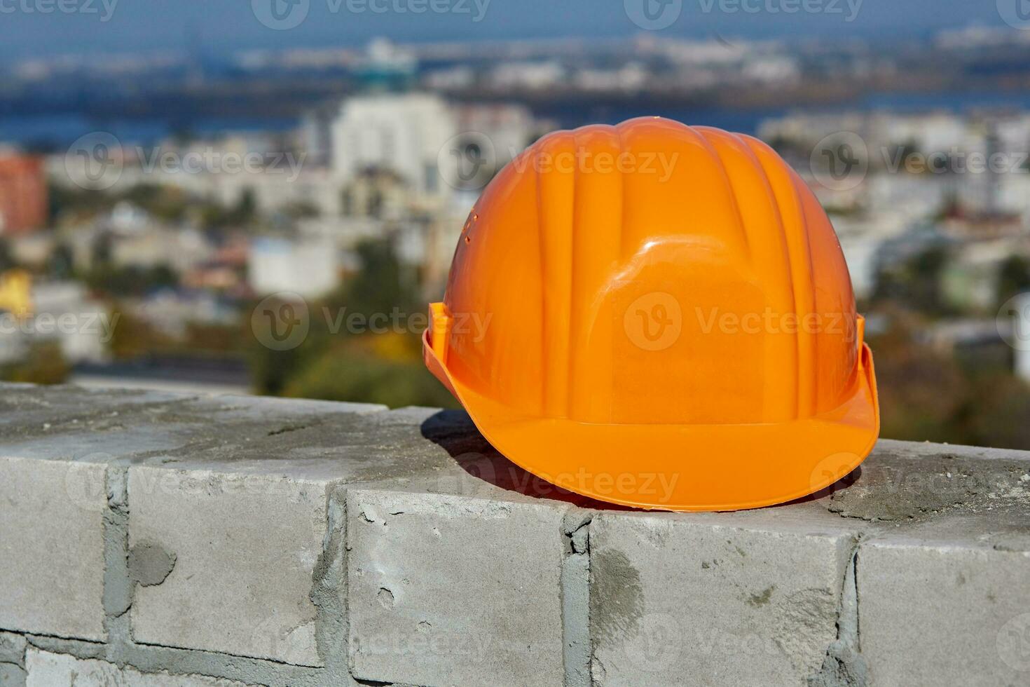 orange plast hård hatt är på en tegel vägg. tak av modern byggnad under konstruktion. naturskön panorama- stadsbild, blå himmel, solig dag foto