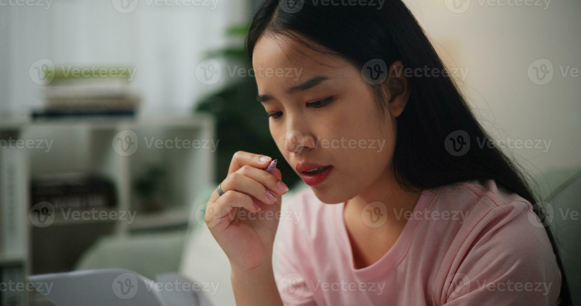 porträtt av ung asiatisk kvinna fokuserade i beräknande budget Sammanträde på soffa på Hem innehav papper skatter räkningar och läsning finansiell information, hem finansiera foto