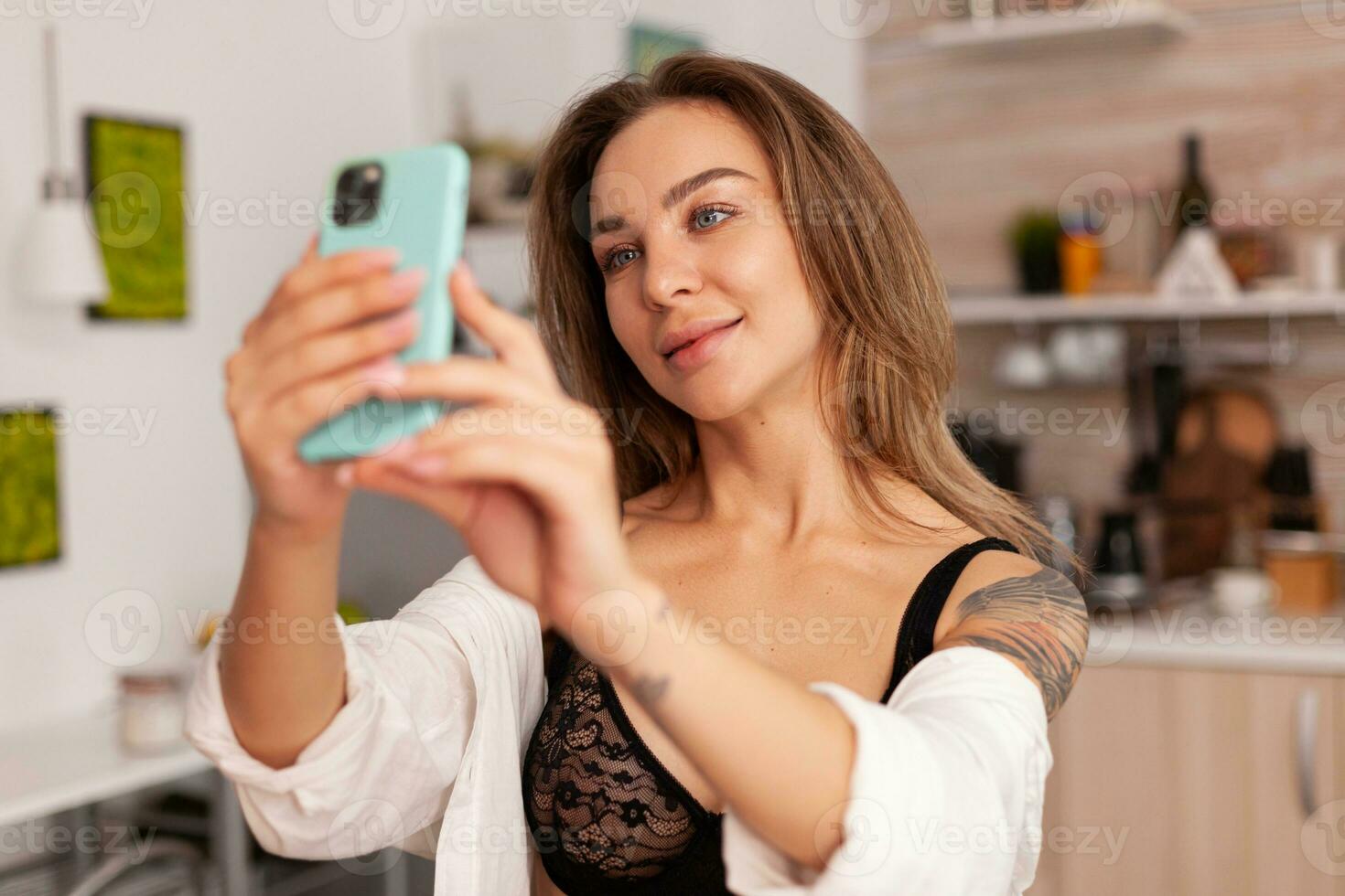 kvinna ejoyer tar foton under frukost bär sexig underkläder. förförisk kvinna med tatueringar använder sig av smartphone bär temping underkläder i de morgon.