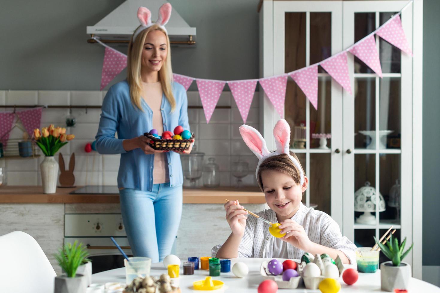 son målar påskägg, mamma tittar och håller en korg. foto