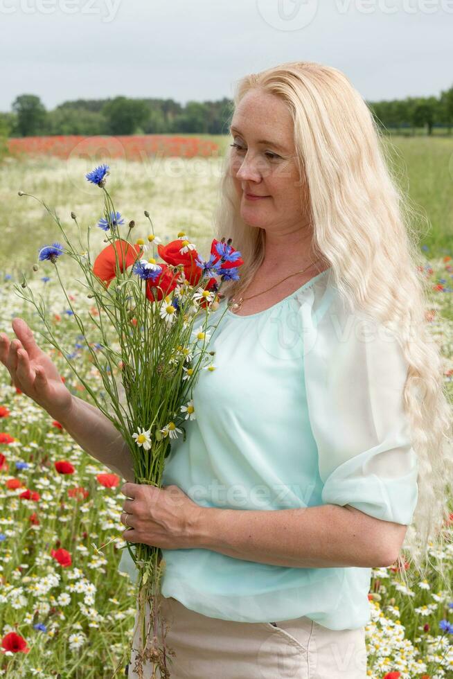 skön medelålders blond kvinna står bland en blommande fält av vallmo foto