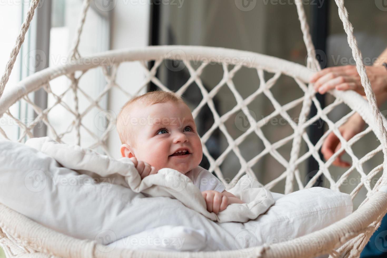 vacker liten flicka som svänger i en hängande stol i sovrummet med sin mamma foto