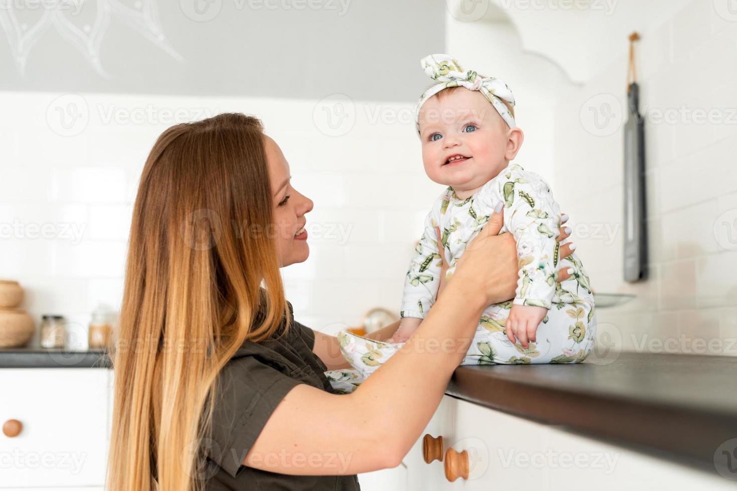 vacker baby flicka sitter, hennes mamma stöder henne foto