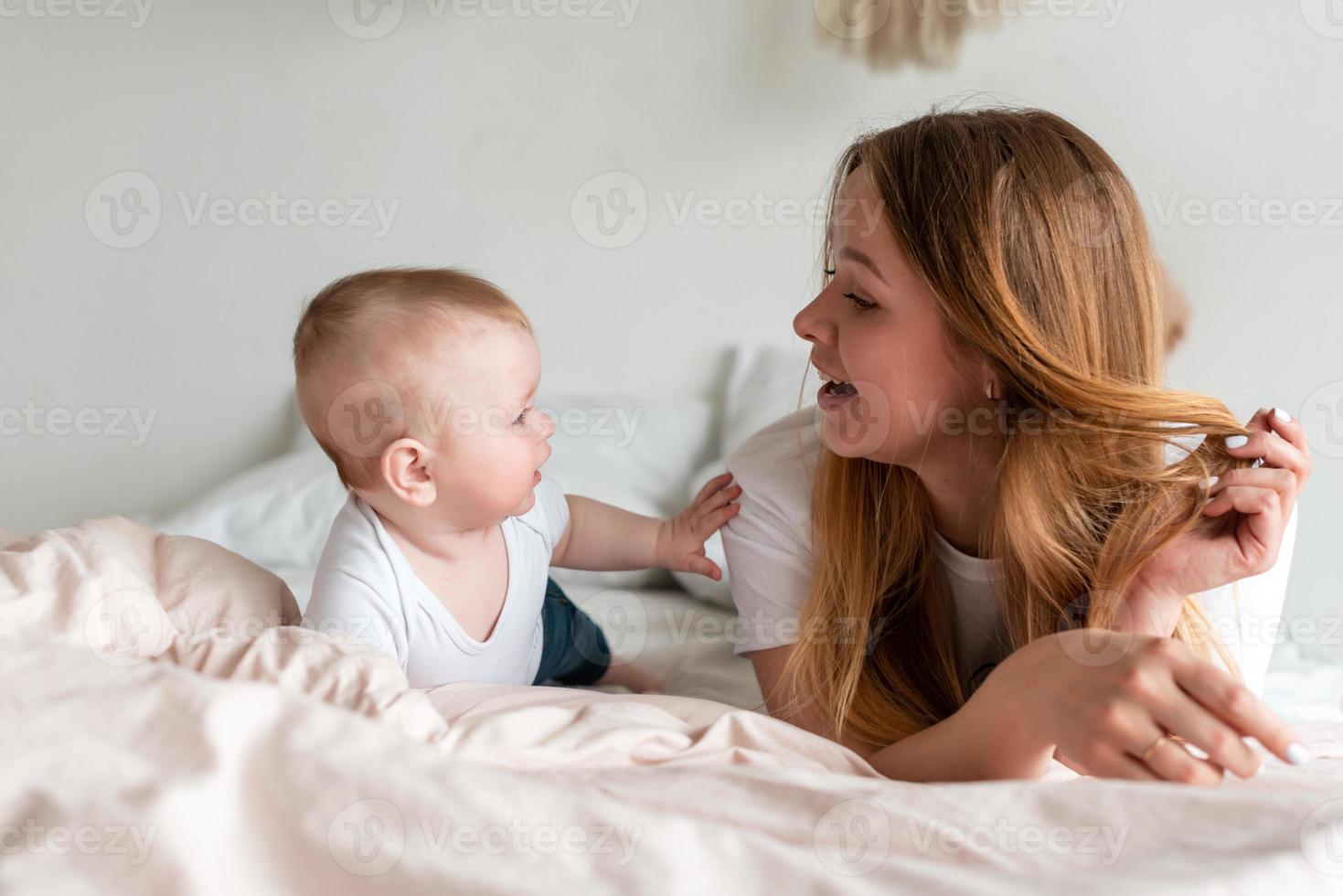 vacker, leende mamma och baby dotter som ligger på sängen och har kul foto