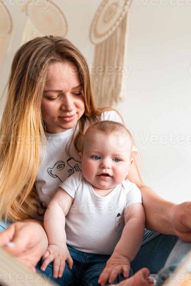 vacker, ung mamma och hennes lilla söta bebis som sitter på sängen. foto