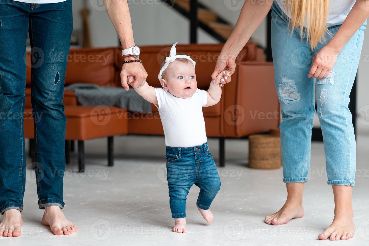 föräldrar håller en söt liten dotter i handtagen, lär henne gå foto