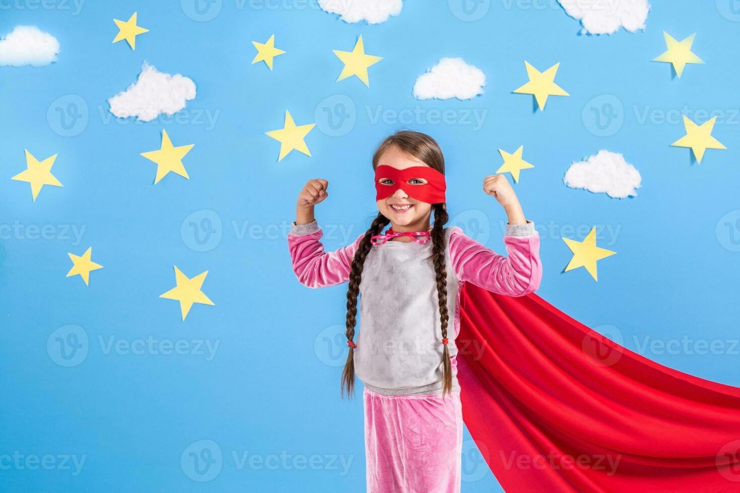 sex år blond flicka klädd tycka om superhjälte har roligt på Hem. unge på de bakgrund av ljus blå vägg. foto