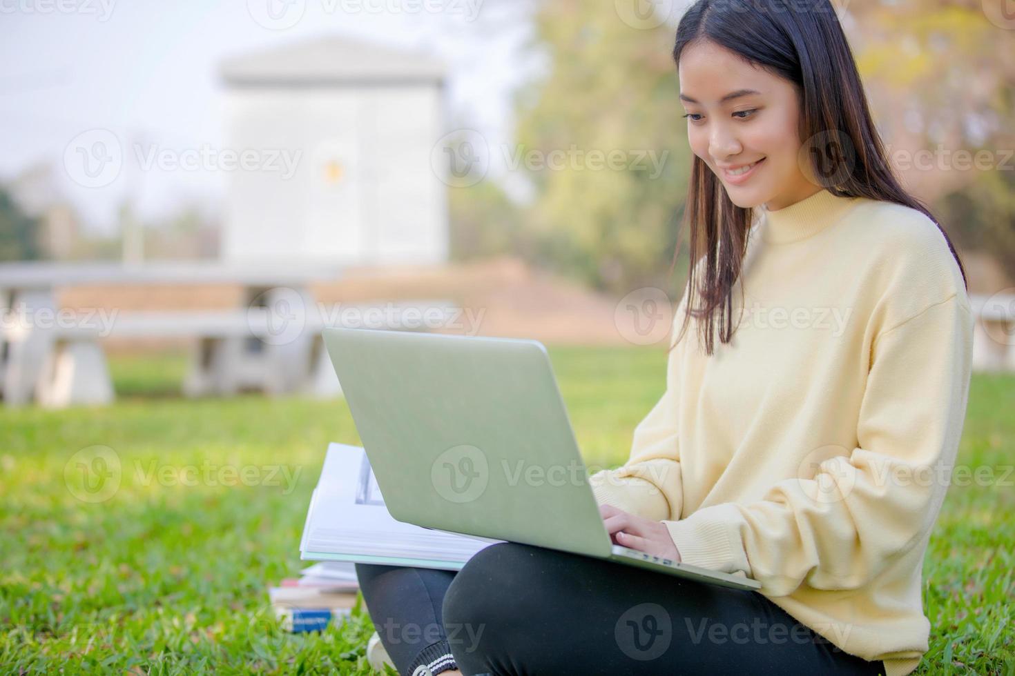 asiatiska kvinnor universitetsstudenter leende och sitter på det gröna gräset och arbetar och läser utomhus tillsammans i en park foto