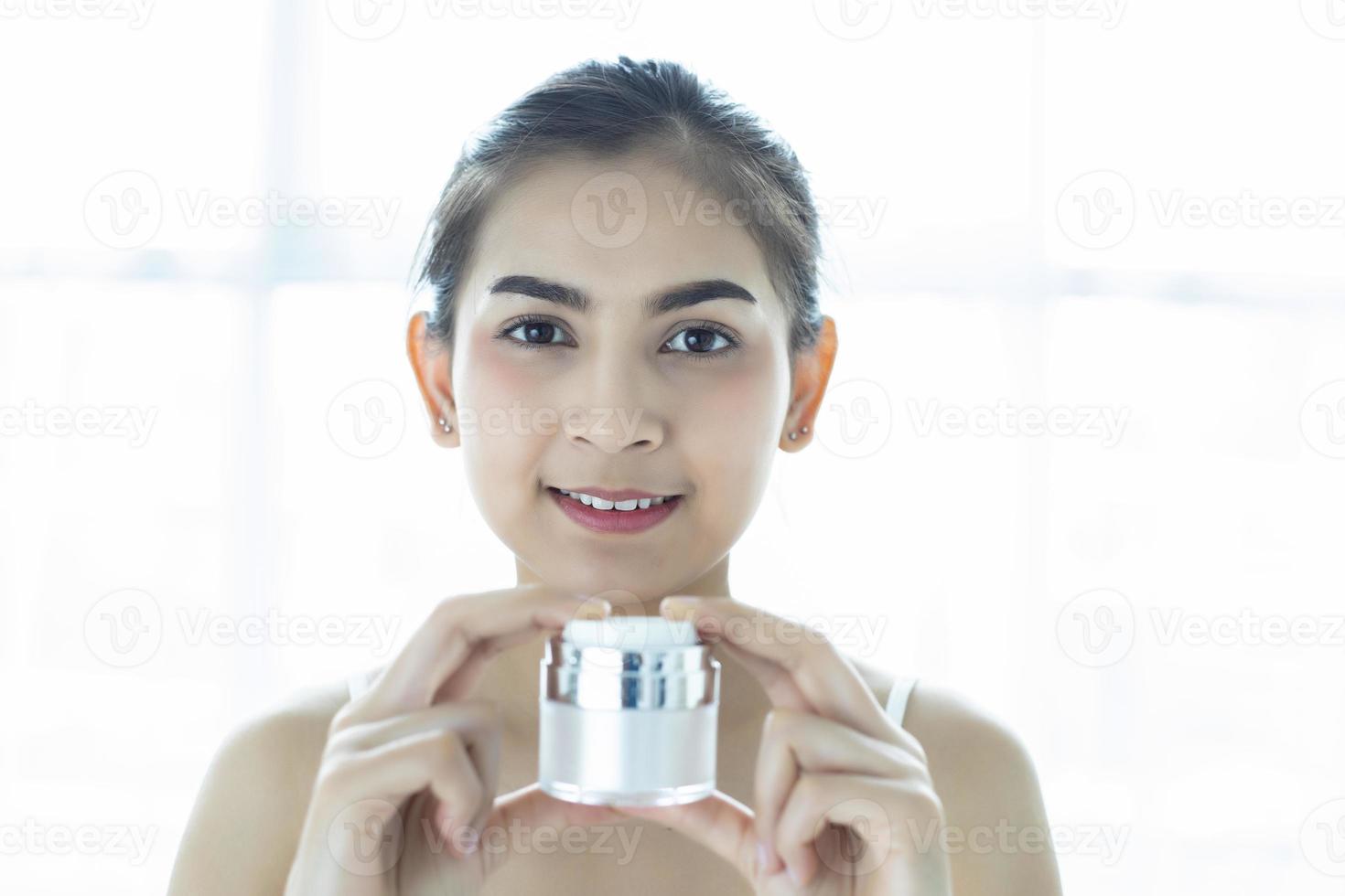 en vacker asiatisk kvinna som använder en hudvårdsprodukt, fuktkräm eller lotion som tar hand om hennes torra hy. fuktkräm i kvinnliga händer. foto