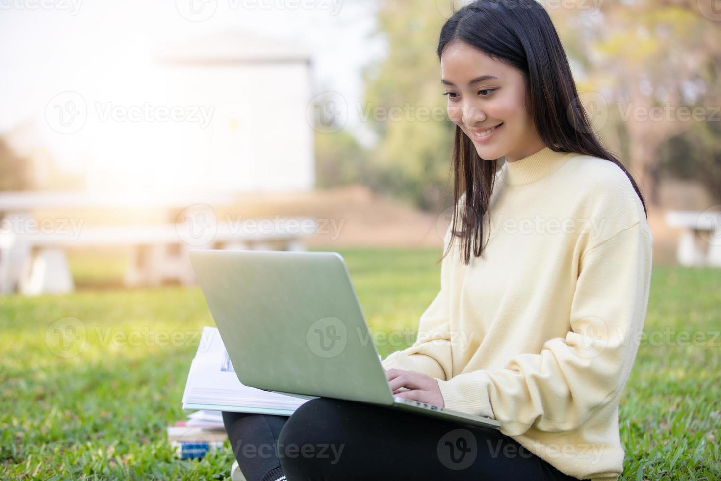 asiatiska kvinnor universitetsstudenter leende och sitter på det gröna gräset och arbetar och läser utomhus tillsammans i en park foto