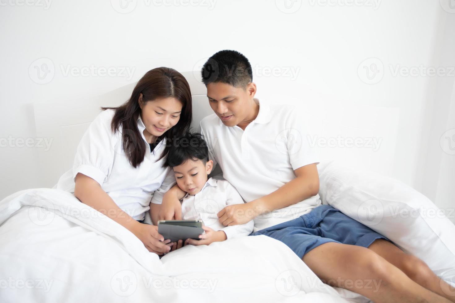 familj och son tittar på och spelar surfplatta på sängen foto