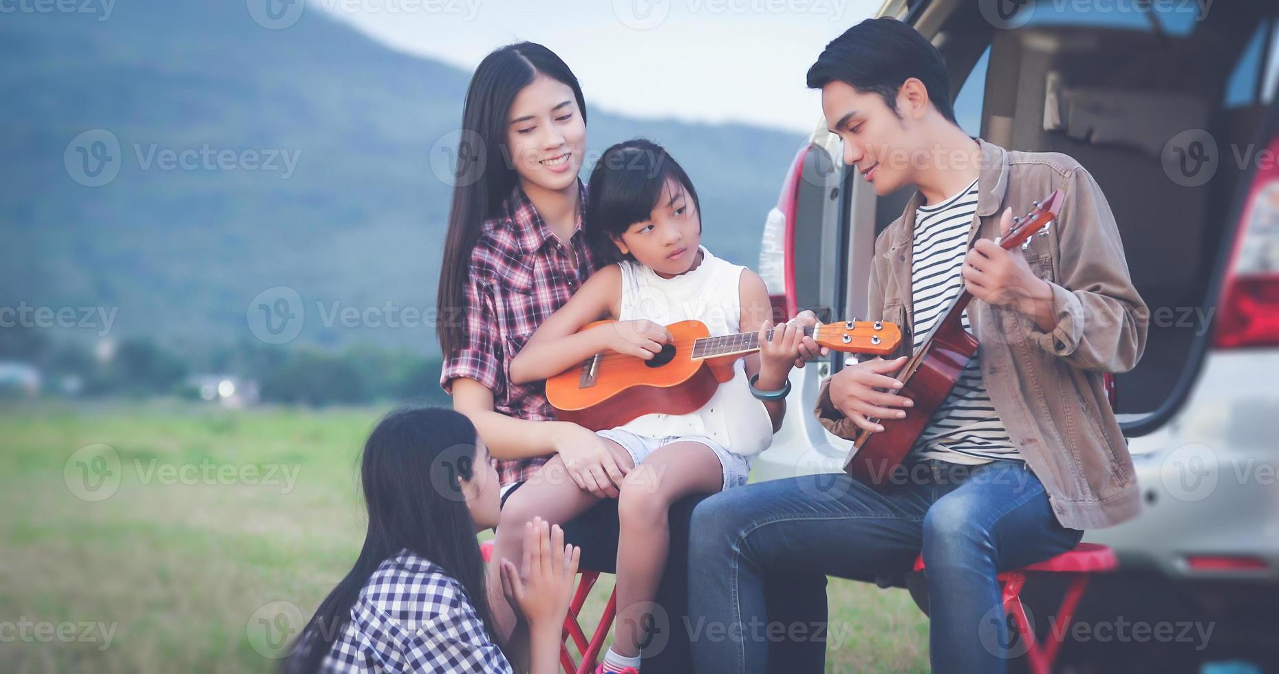 glad liten flicka som leker ukulele med asiatisk familj som sitter i bilen för att njuta av roadtrip och sommarlov foto