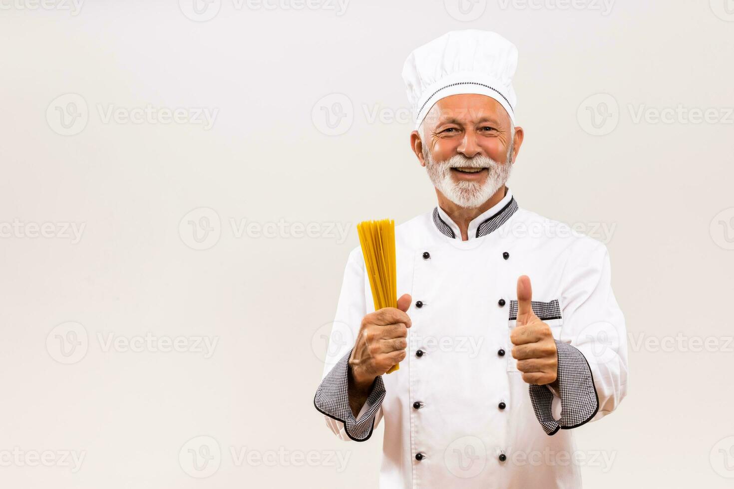 porträtt av senior kock innehav spaghetti och som visar tumme upp på grå bakgrund. foto