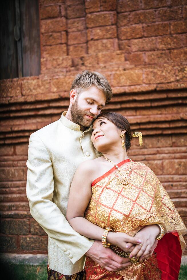 asiatisk brud och kaukasisk brudgum har romantisk tid med thailändsk klänning foto