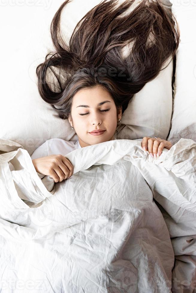 ung vacker brunettkvinna som sover i sängen foto