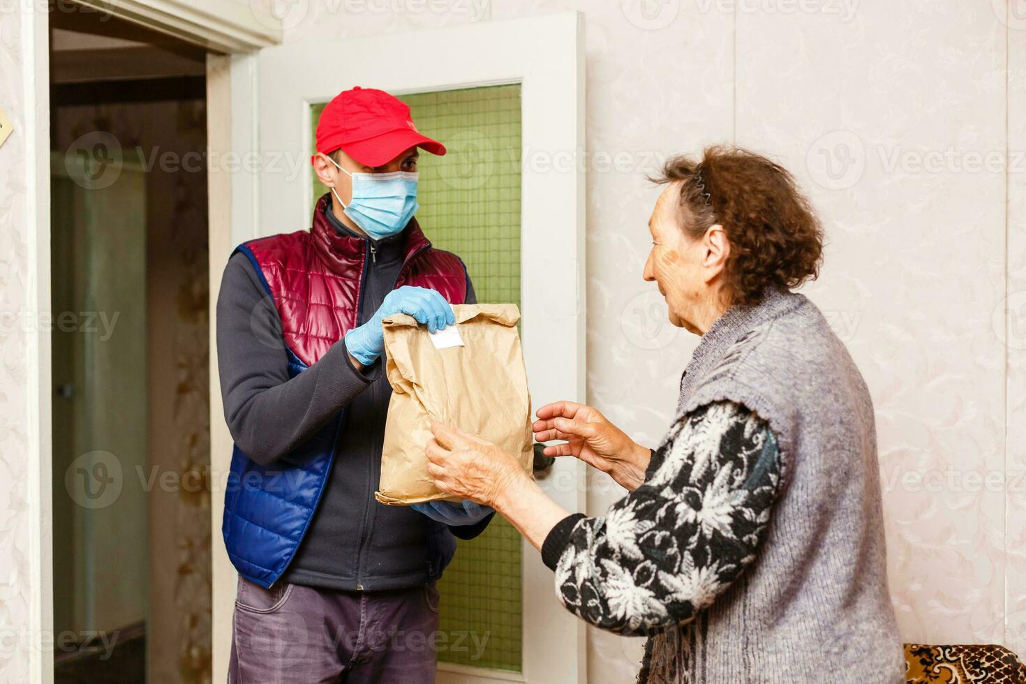 ung manlig volontär- i mask ger ett äldre kvinna lådor med mat nära henne hus. son man hjälper en enda äldre mor. familj Stöd, omtänksam. i karantän, isolerat. coronavirus covid19. donation foto