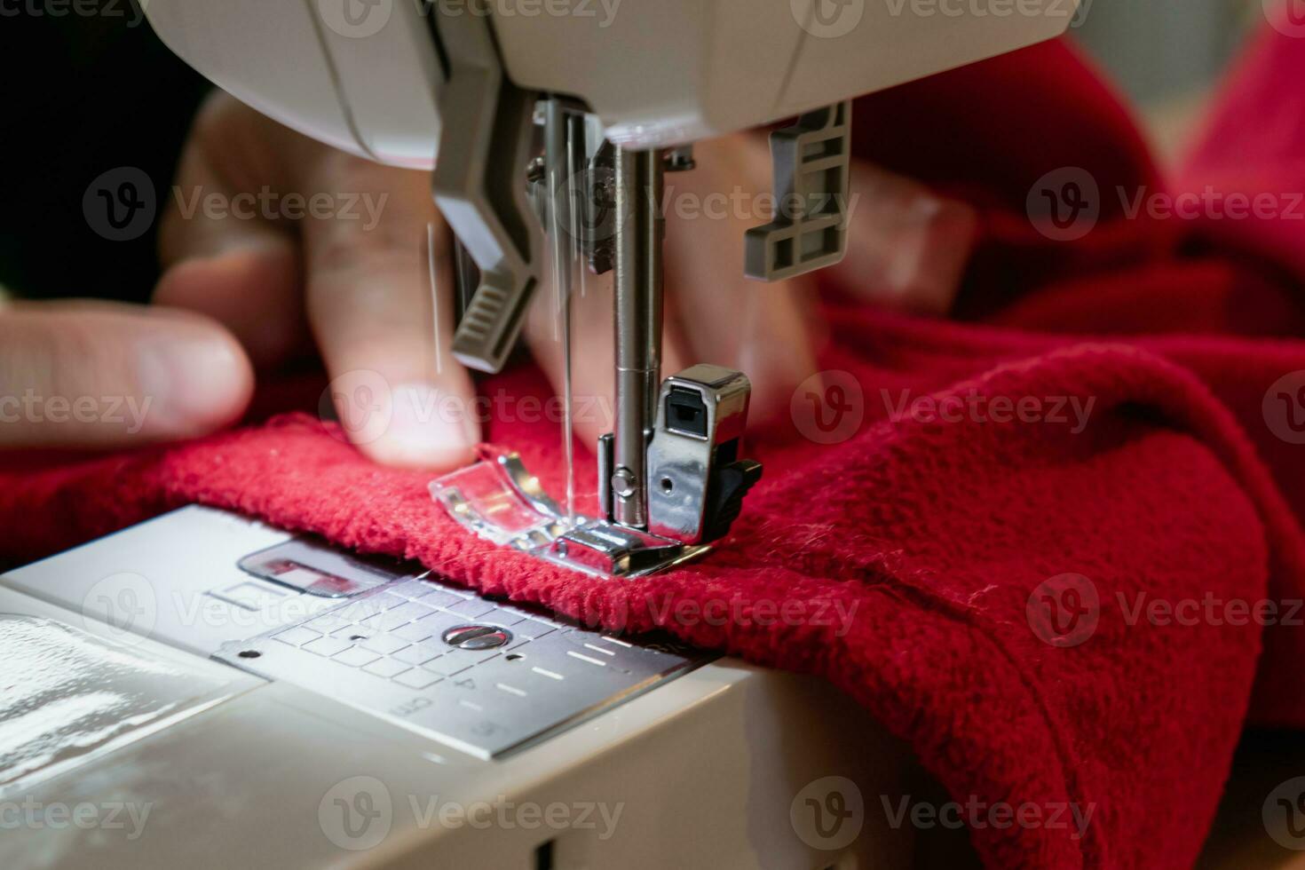 man använder sig av en sömnad maskin med en röd plagg, för reparera arbete, anpassning, skapande, upcycling foto