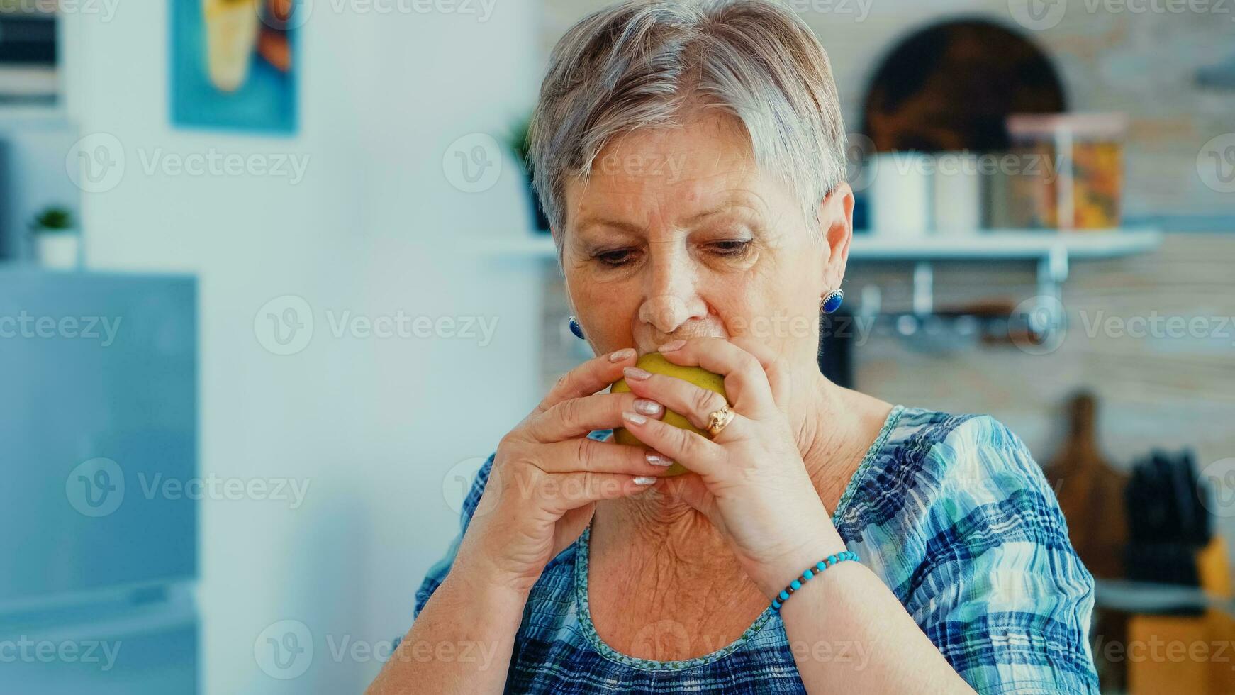 Lycklig senior kvinna äter friska grön äpple i kök under frukost. Lycklig färsk organisk livsstil med Bra mat. glad positiv äkta porträtt foto