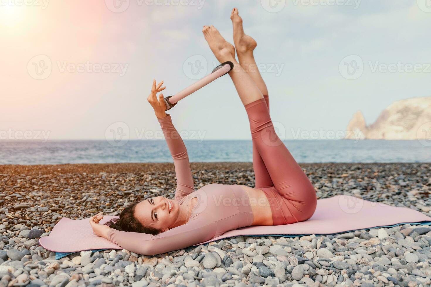 kvinna hav pilates. sportig Lycklig mitten åldrig kvinna praktiserande kondition på strand nära hav, leende aktiva kvinna Träning med ringa på yoga matta utanför, njuter friska livsstil, harmoni och meditation foto