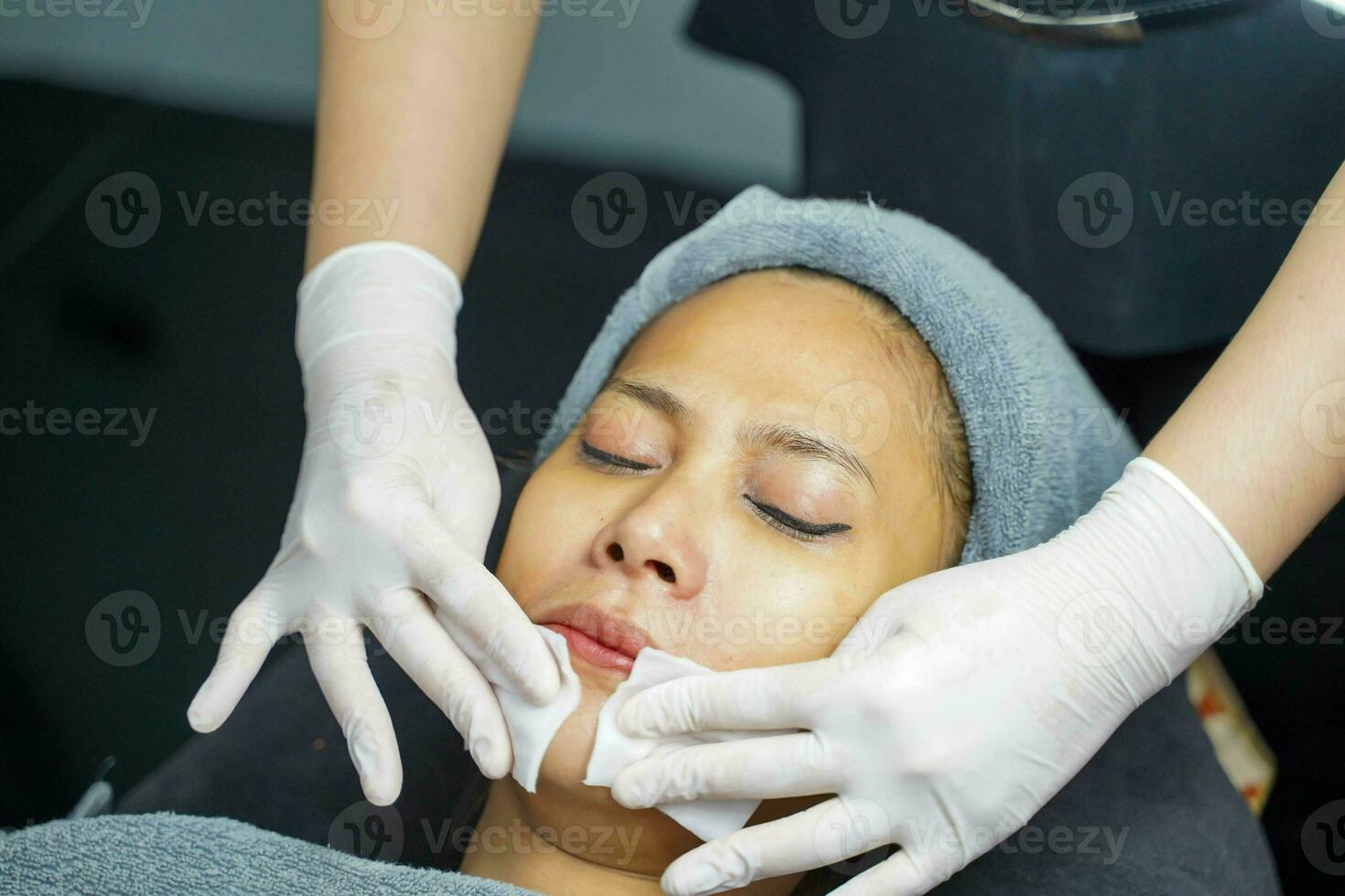kosmetolog använda sig av en bomull vaddera till rena på kvinna klient ansikte i skönhet klinik. foto