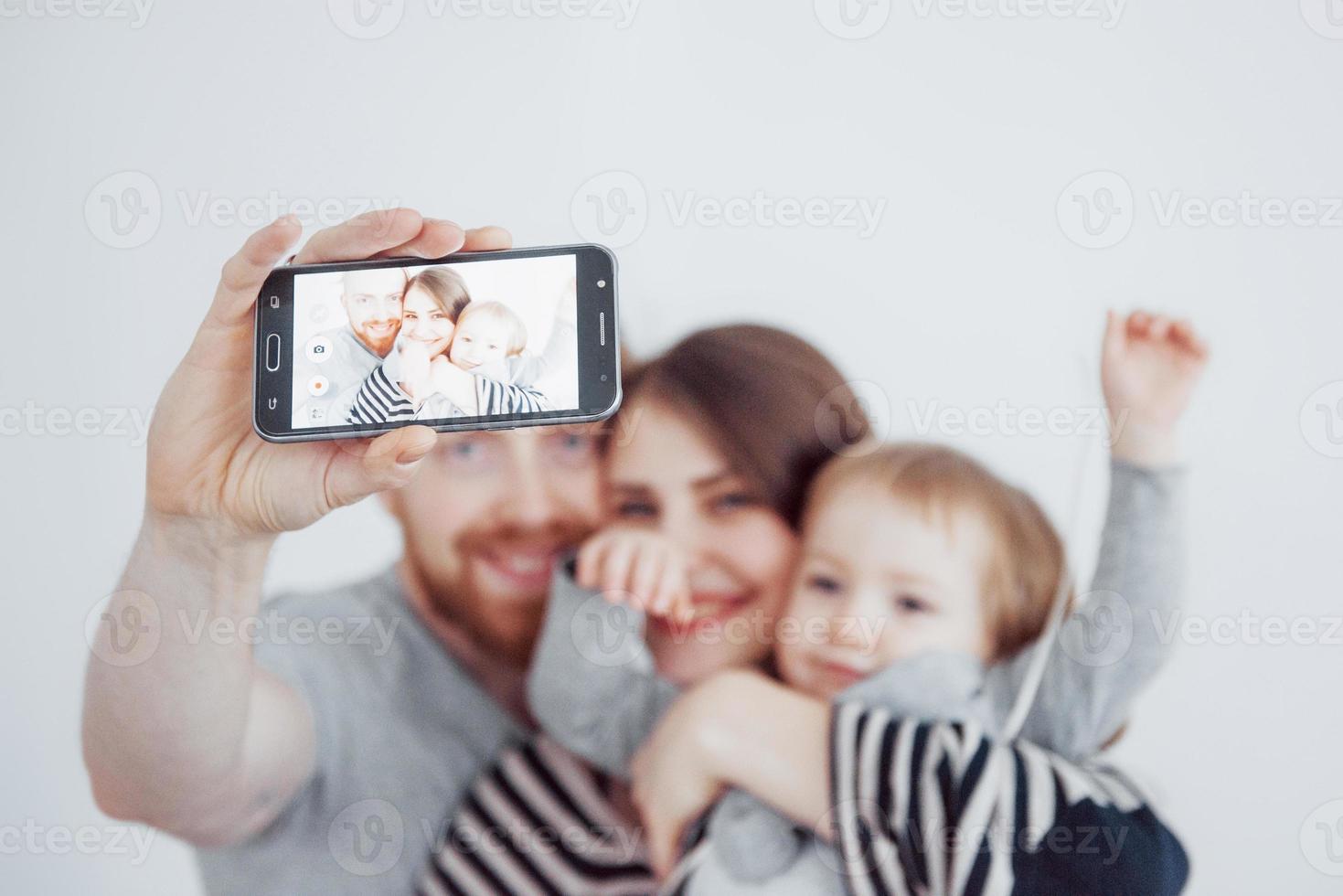 familj, semester, teknik och människor - leende mamma, pappa och liten flicka gör selfie med kamera över vit bakgrund foto