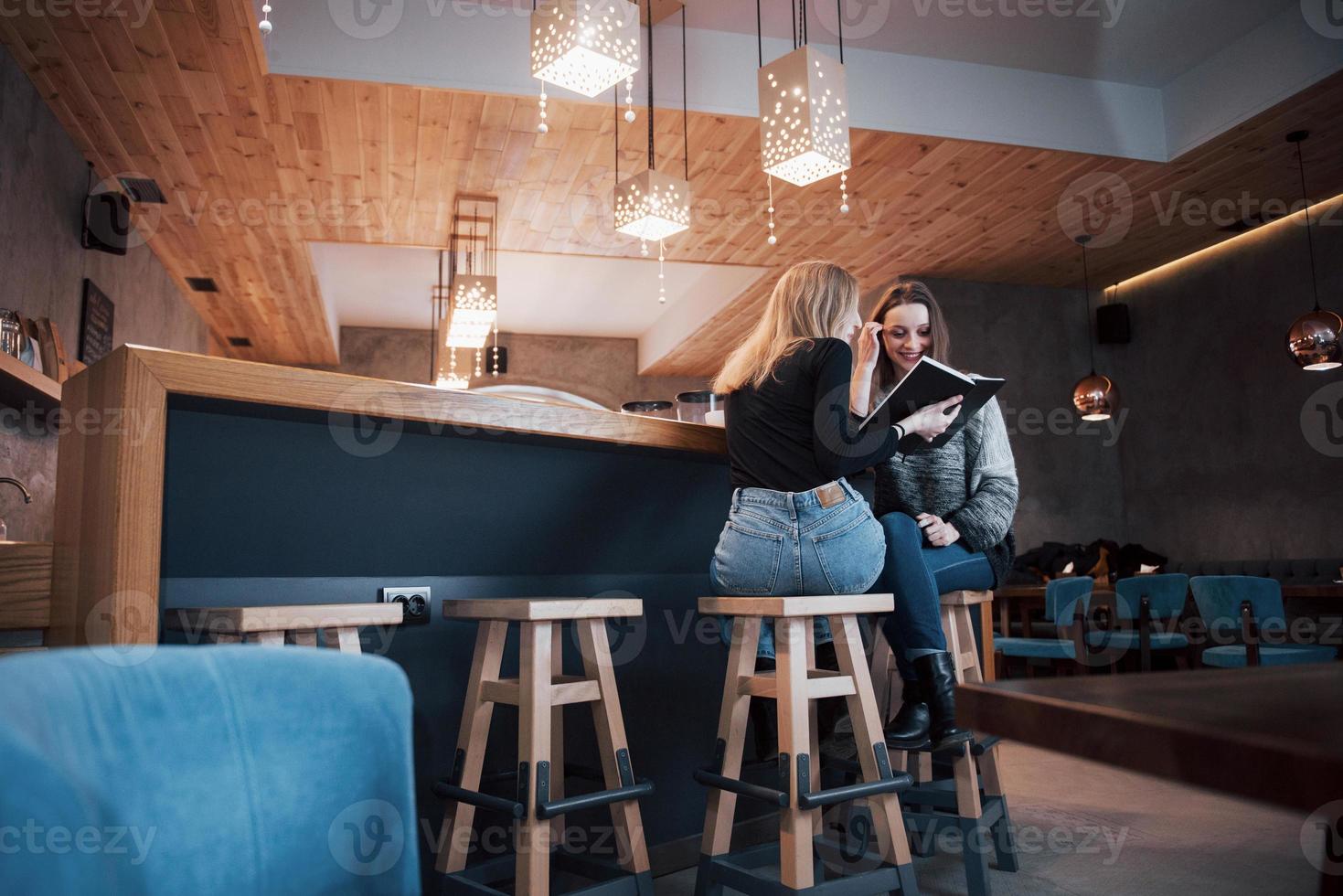 två tjejer absorberades av att läsa bok under pausen i caféet. söta härliga unga kvinnor läser bok och dricker kaffe foto