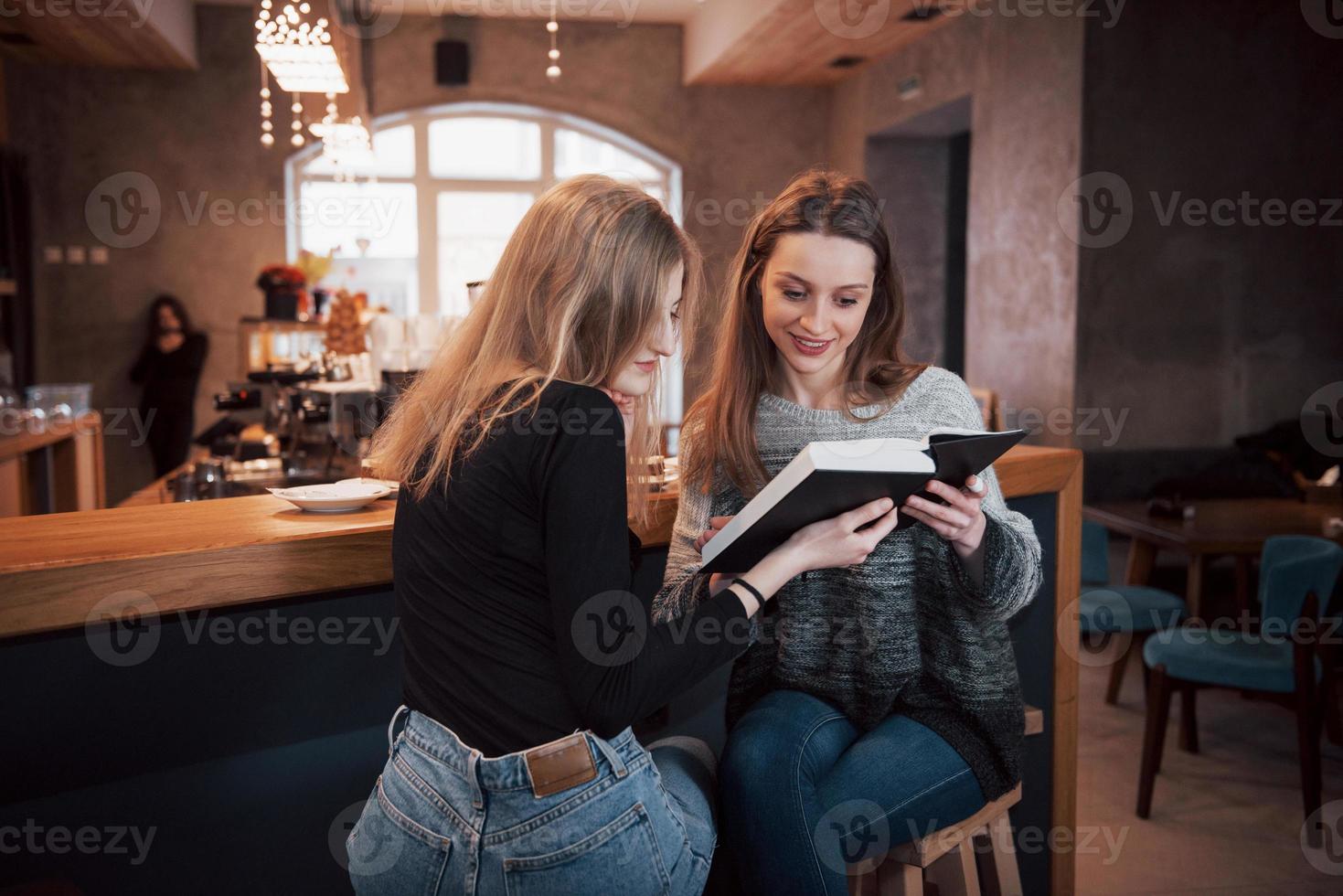 två tjejer absorberades av att läsa bok under pausen i caféet. söta härliga unga kvinnor läser bok och dricker kaffe foto