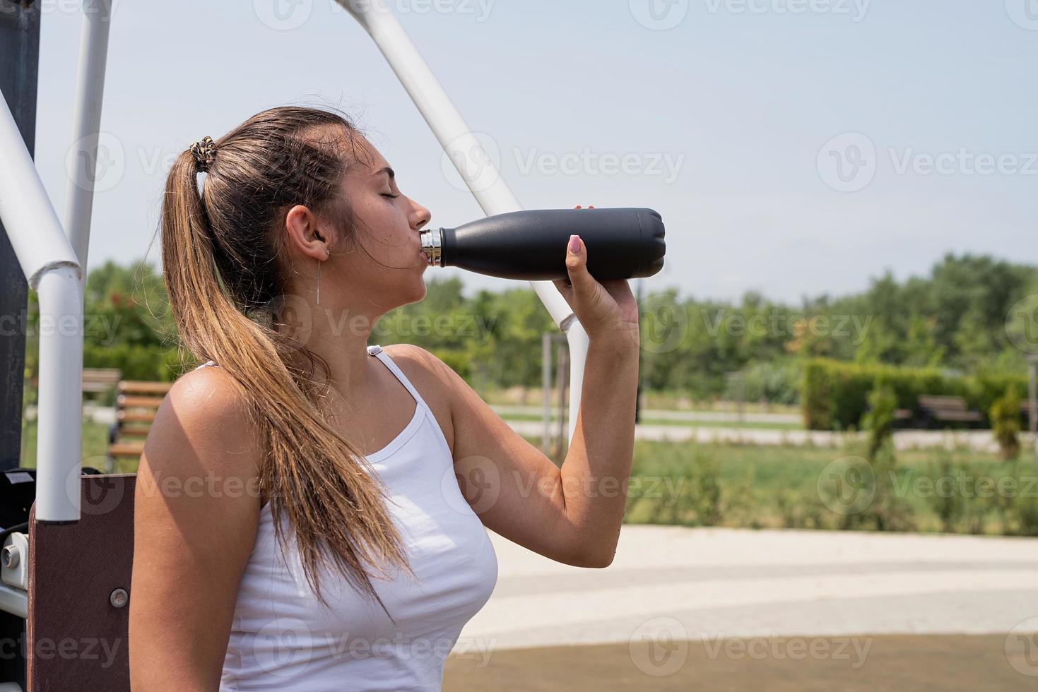 glad kvinna som tränar på idrottsplatsen i solig sommardag, dricker vatten från flaskan, har vila foto