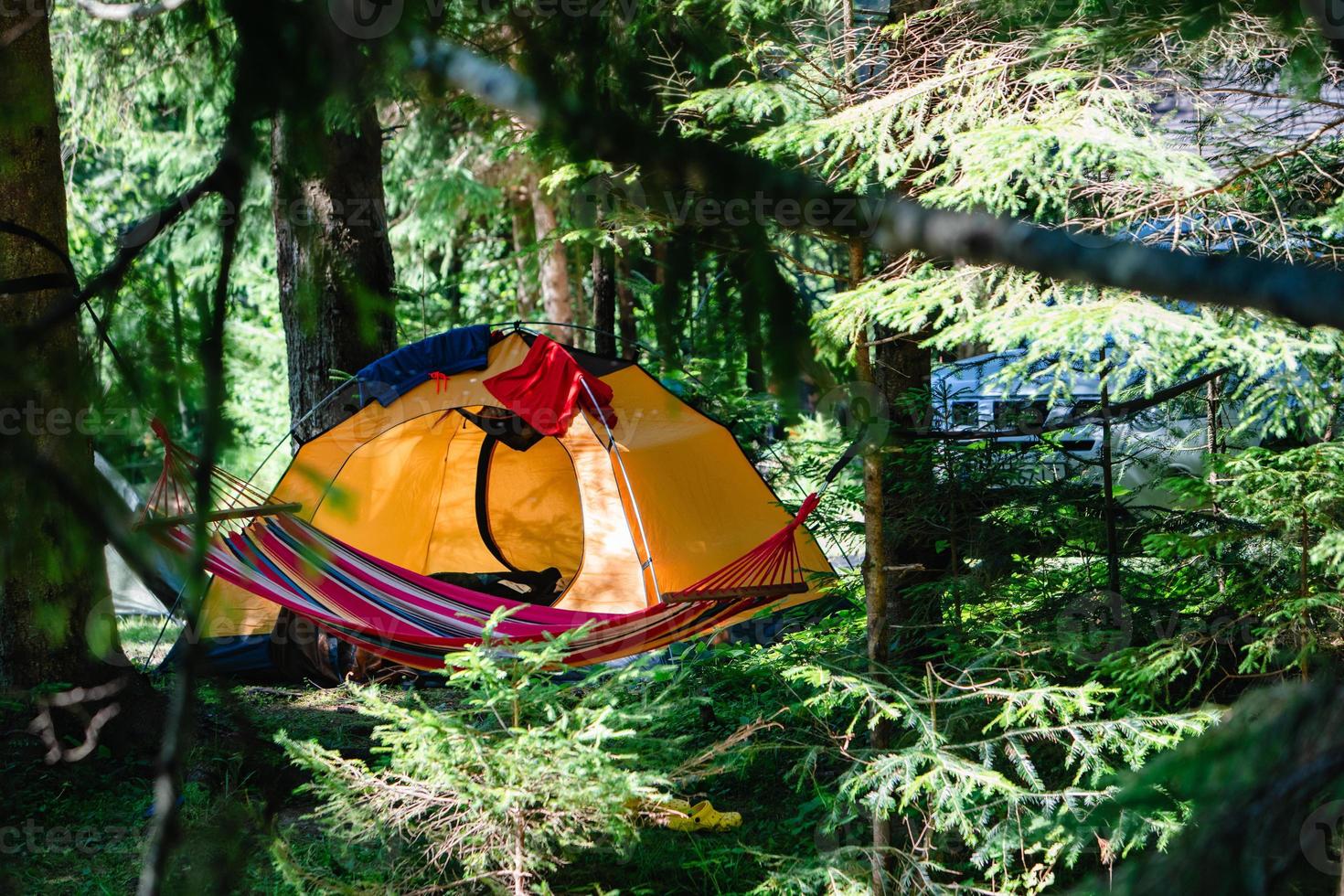 gult tält i skogen med hängmatta och bil på bakgrunden foto