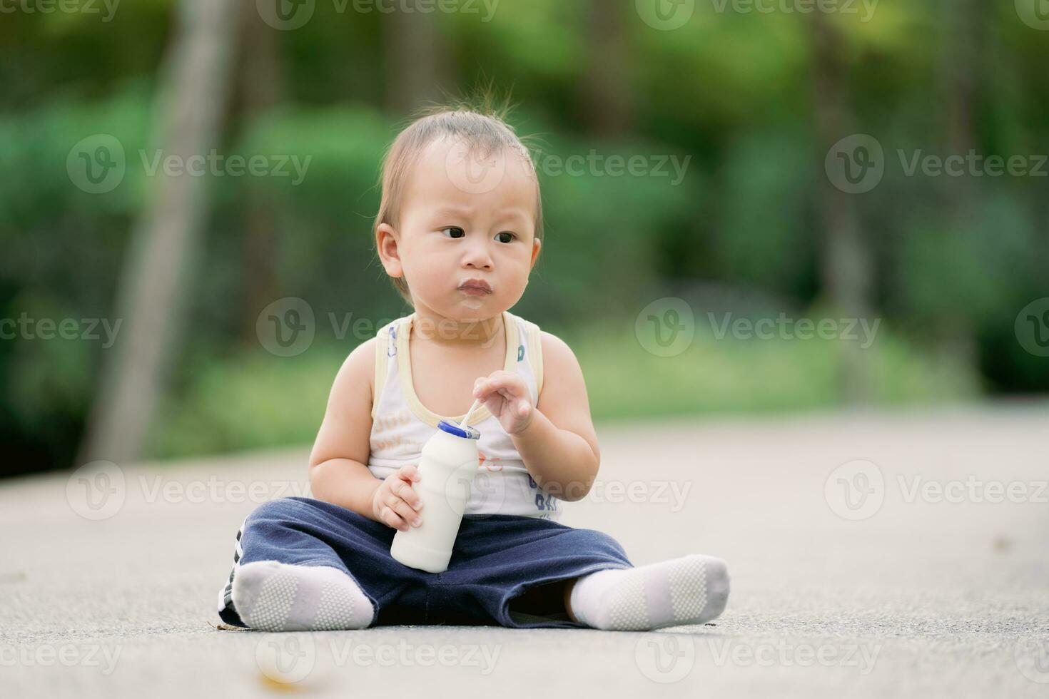 asiatisk bebis pojke dricka mjölk från flaska med rör. litet barn 1 år gammal Sammanträde på golv. de barnets mun var täckt med mjölk. foto