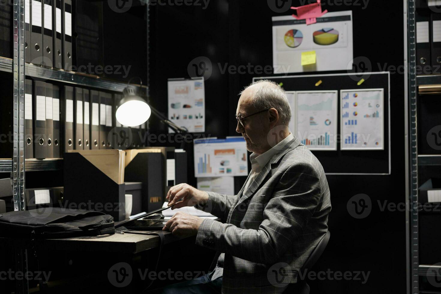 äldre affärsman stänga av bärbar dator på jobb framställning till lämna arbetsplats. förvaltning bokföring verkställande omgiven förbi finansiell fil statistik data flödesscheman i lagring rum foto