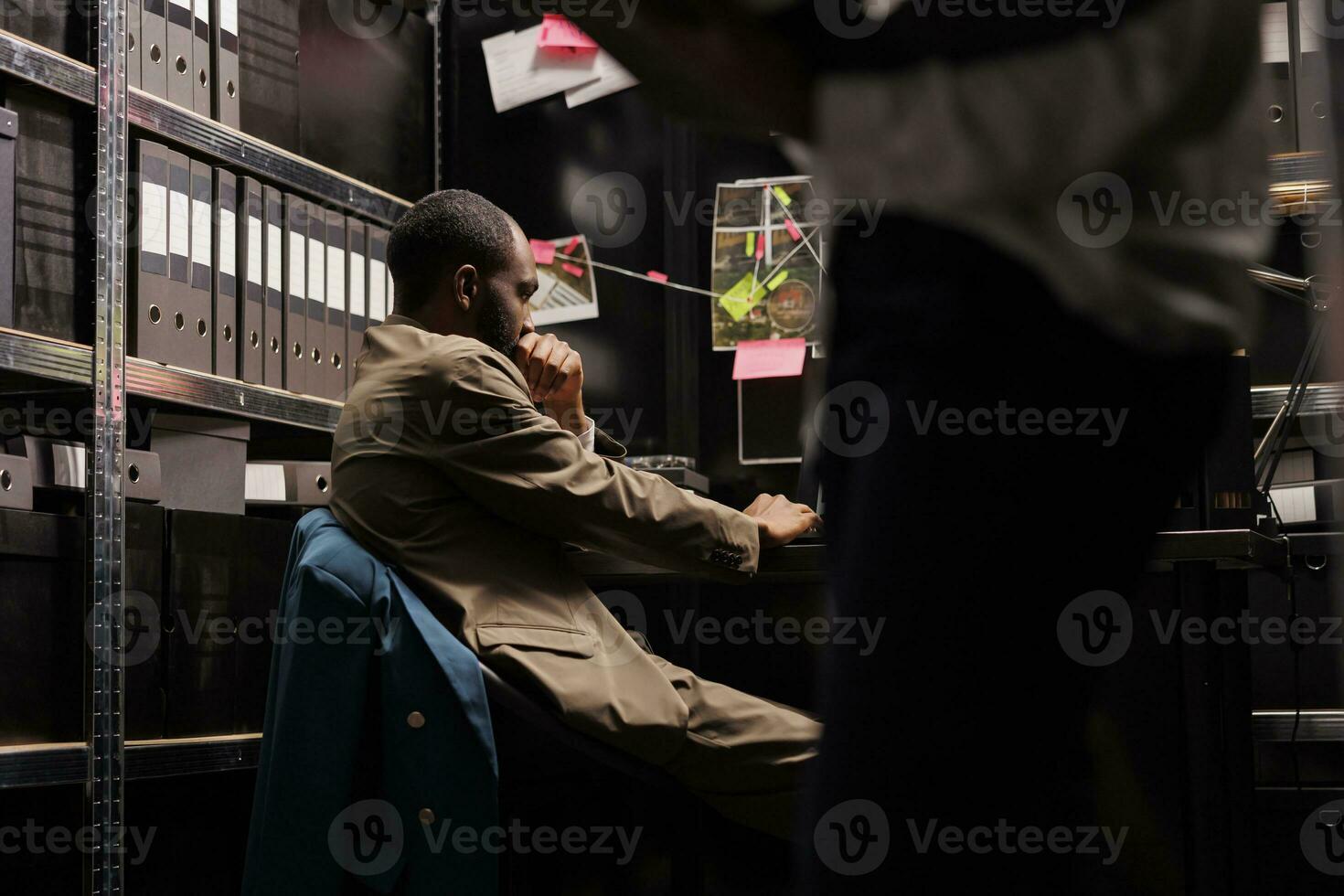 afrikansk amerikan detektiv- arbetssätt på arbetsplats skrivbord i byrå kontor. bekymrad forskare brainstorming, tänkande handla om lösning brottslighet medan Sammanträde på tabell på natt tid foto