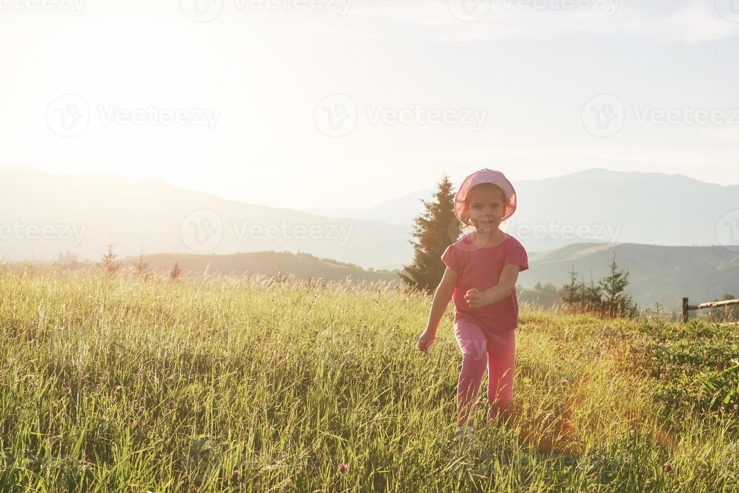söt glad liten flicka leker utomhus tidigt på morgonen i gräsmattan och beundrar bergen. kopiera utrymme för din text foto