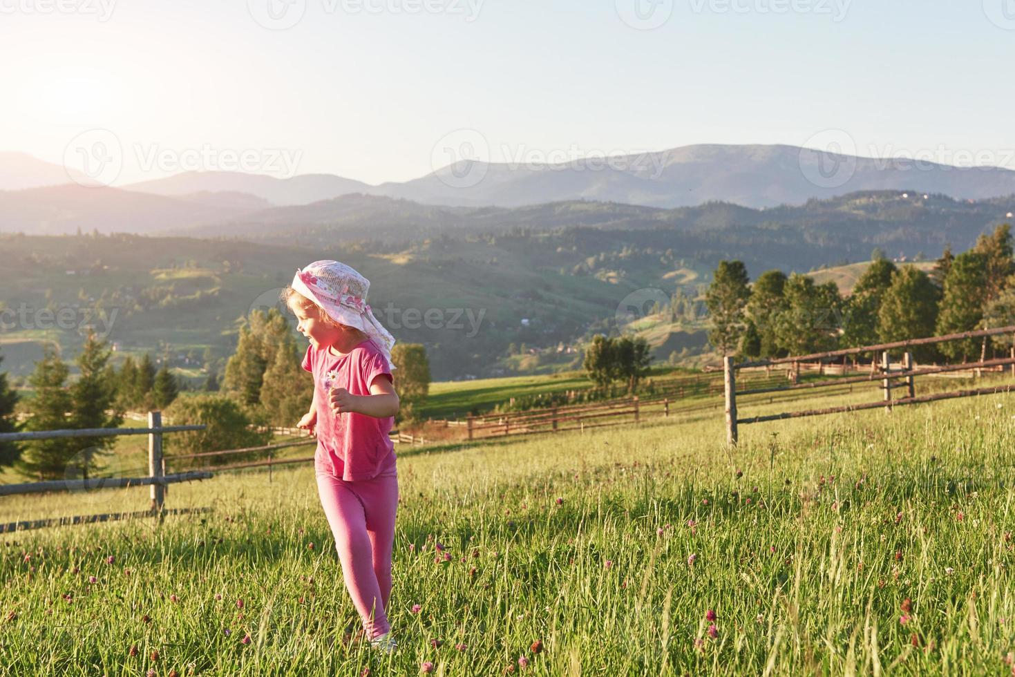 söt glad liten flicka leker utomhus i gräsmattan och beundrar bergen. kopiera utrymme för din text foto