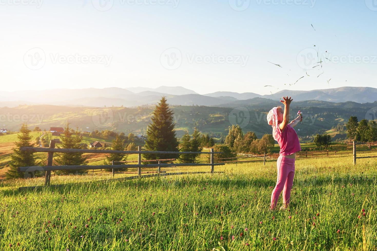 söt glad liten flicka leker utomhus tidigt på morgonen i gräsmattan och beundrar bergen. kopiera utrymme för din text foto