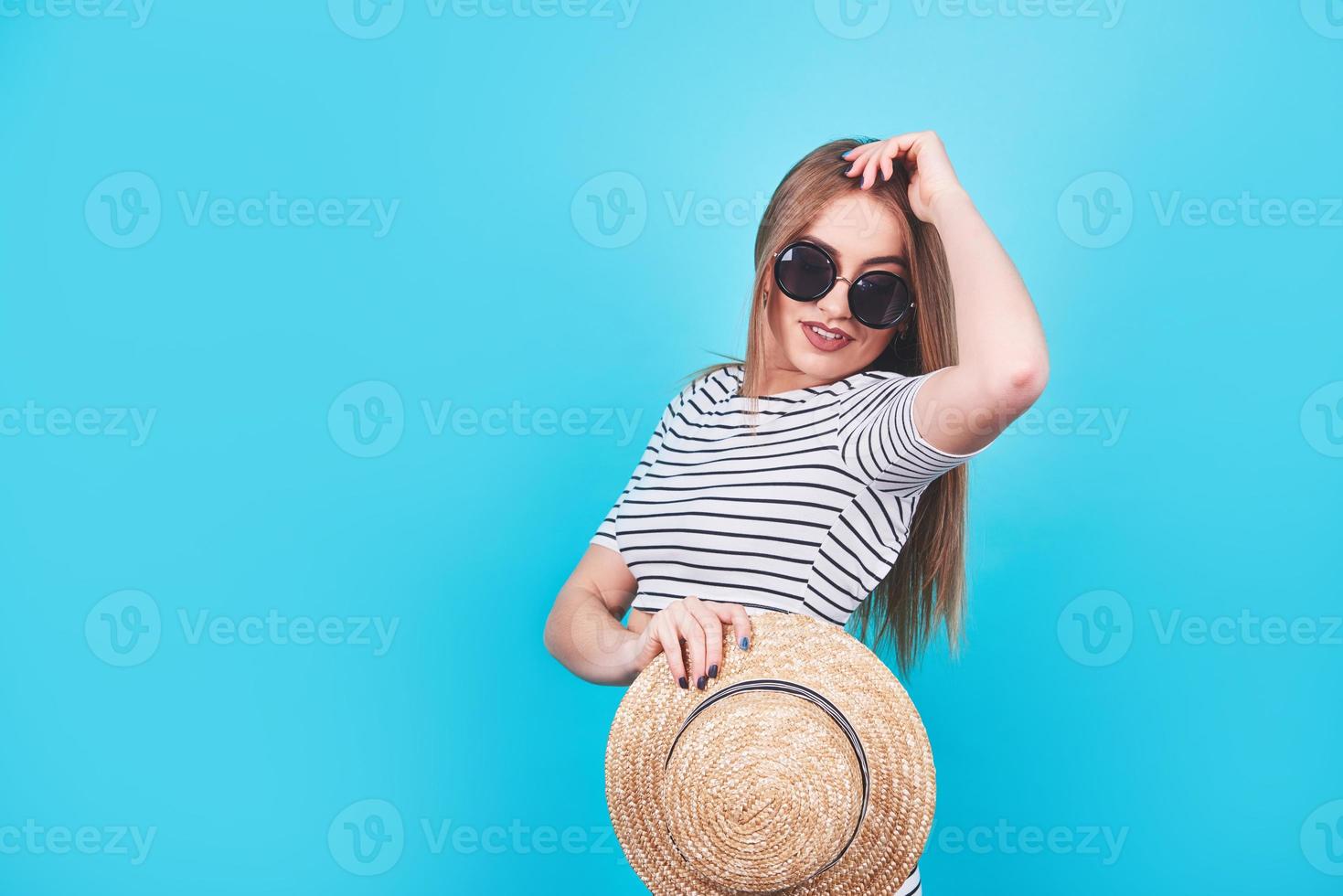 attraktiv tjej i vita och svarta ränder, hatt, solglasögon, känslomässigt öppnad mun på en ljusblå bakgrund med en perfekt kropp. isolerat. studioskott foto