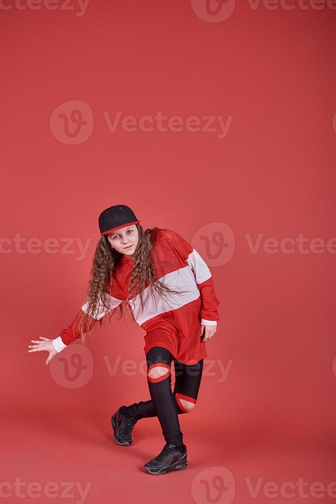 ung vacker söt flicka som dansar på röd bakgrund, modern smal hip-hop stil tonårsflicka som hoppar foto