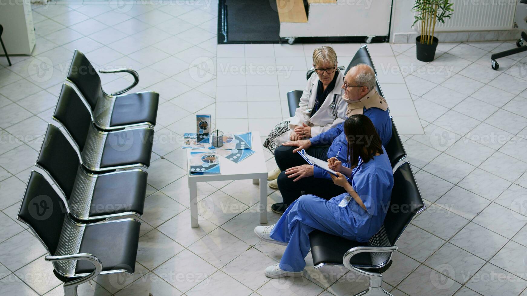 senior läkare läkare och assistent portion äldre patient till ta av cervical nacke krage under kolla upp besök samråd i sjukhus väntar område. gammal man tar emot medicin Stöd foto