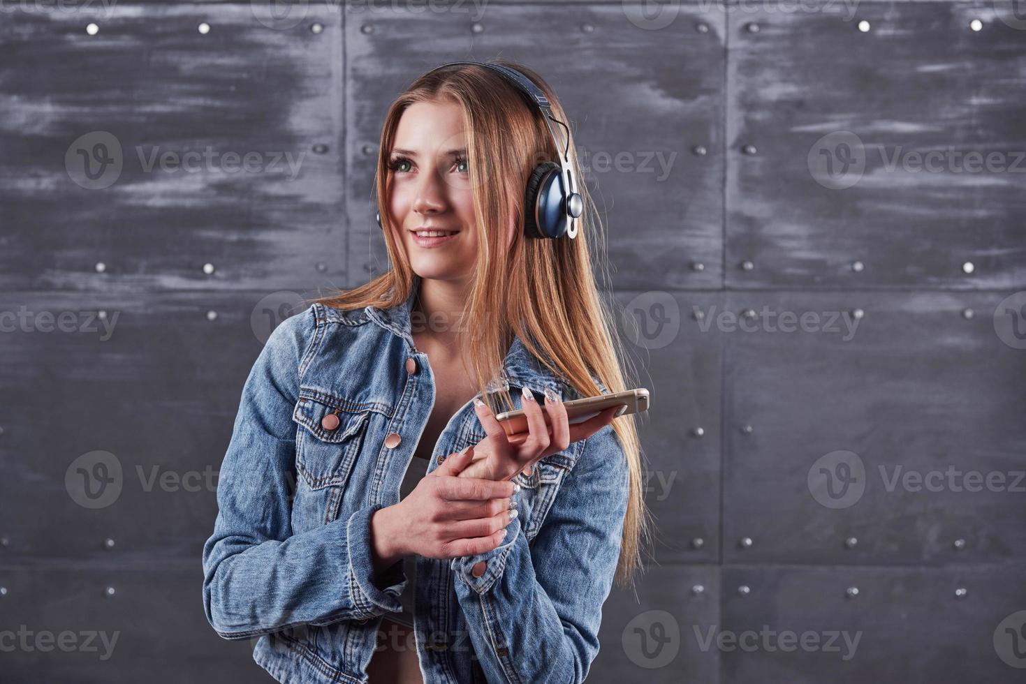 mode, kläder, människor koncept. attraktiv sexig ung kvinna med jeansjacka. flicka poserar i studion lyssnar på musik i hörlurar foto