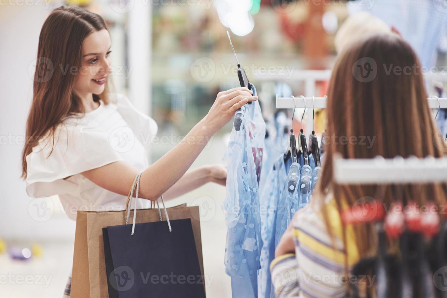 shoppingterapi i aktion. bakifrån av två vackra kvinnor med shoppingkassar som tittar på varandra med leende medan de går i klädbutiken foto