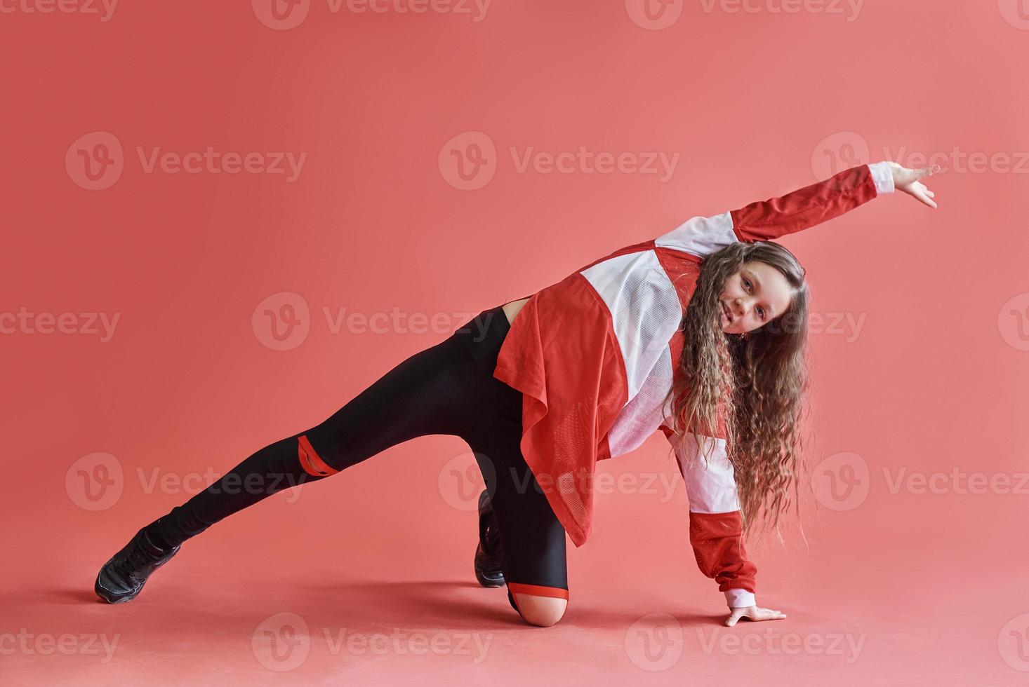 ung vacker söt flicka som dansar på röd bakgrund, modern smal hip-hop stil tonårsflicka som hoppar foto