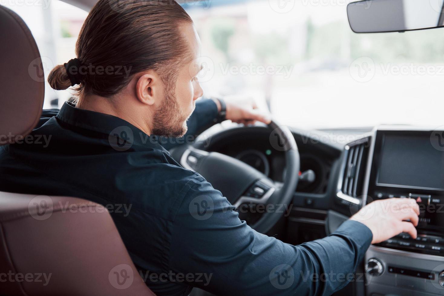 självsäker ung affärsman sitter vid ratten i sin nya bil foto