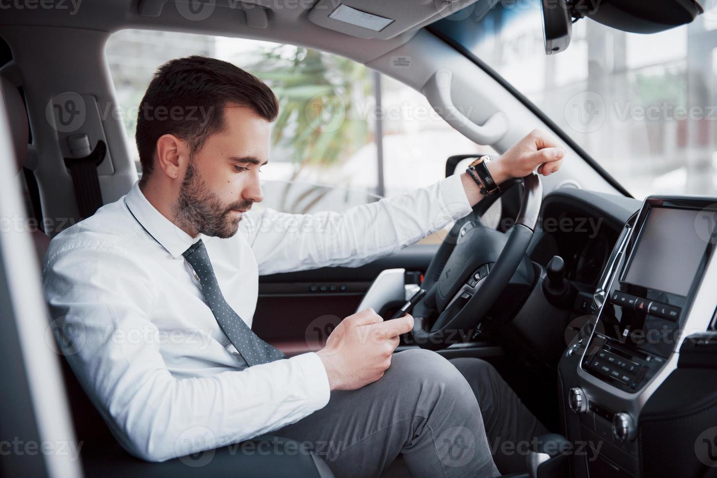 nöjd ung affärsman som tittar på mobiltelefonen medan han kör bil foto