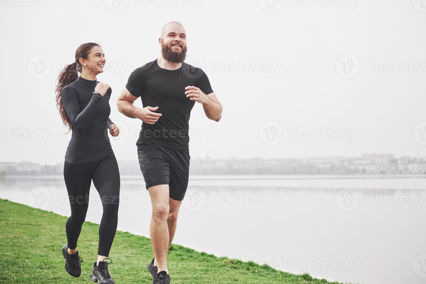 par joggar och springer utomhus i parken nära vattnet. ung skäggig man och kvinna som tränar tillsammans på morgonen foto