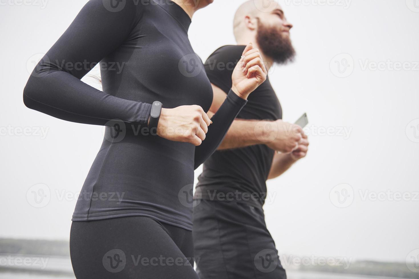 par joggar och springer utomhus i parken nära vattnet. ung skäggig man och kvinna som tränar tillsammans på morgonen foto