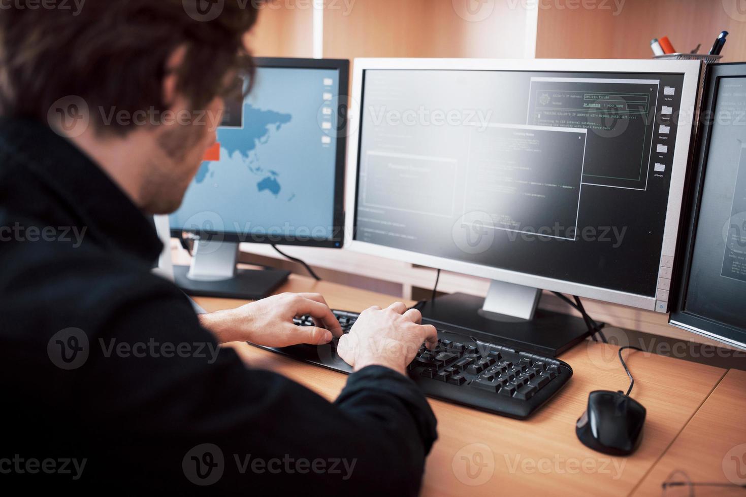 den unga farliga hackaren bryter ner regeringstjänster genom att ladda ner känslig data och aktivera virus. en man använder en bärbar dator med många bildskärmar foto
